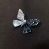 Broche papillon asymétrique, ailes nacrées et cristaux verts et violets, tête en perle