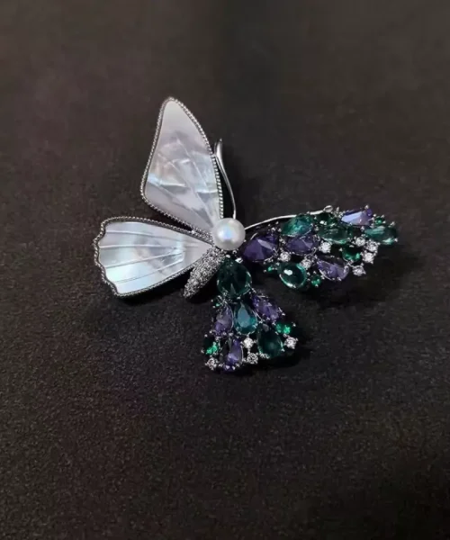 Broche papillon asymétrique, ailes nacrées et cristaux verts et violets, tête en perle