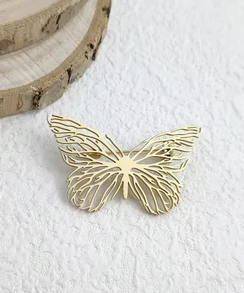 Broche papillon en or ajourée en acier inoxydable posée sur bois clair