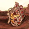 Broche papillon rouge vue de profil, strass rubis et navettes ambrées sur monture dorée ajourée