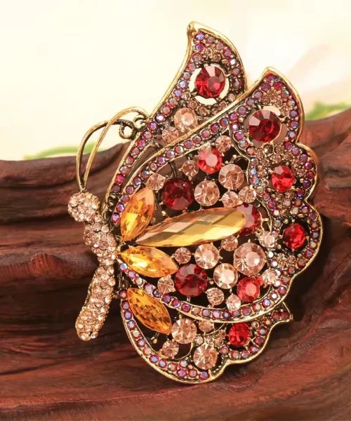 Broche papillon rouge vue de profil, strass rubis et navettes ambrées sur monture dorée ajourée