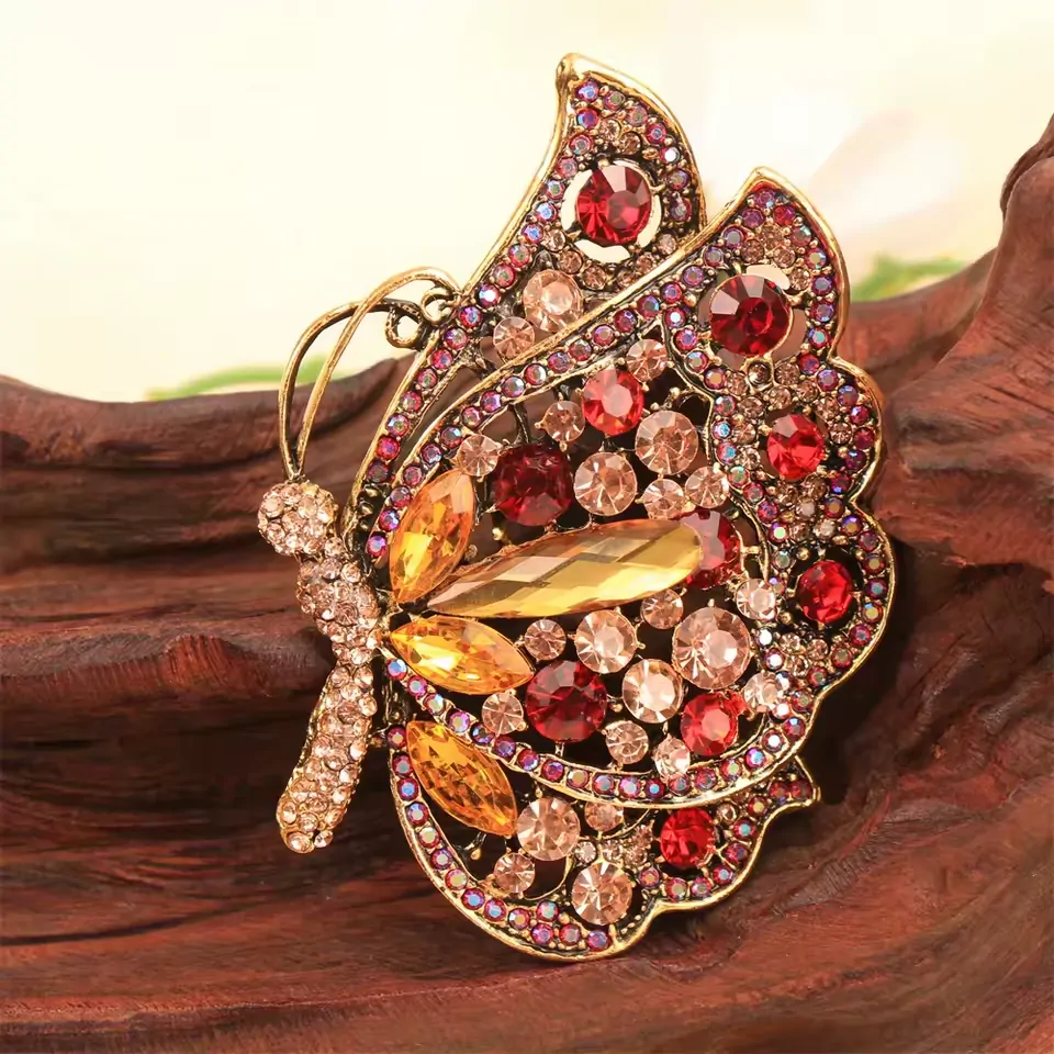 Broche papillon rouge vue de profil, strass rubis et navettes ambrées sur monture dorée ajourée
