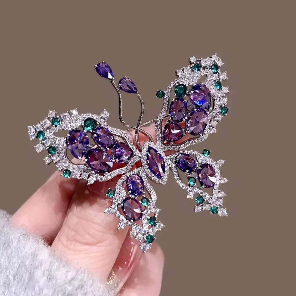 Broche papillon violette tenue en main, pierres violettes et vertes