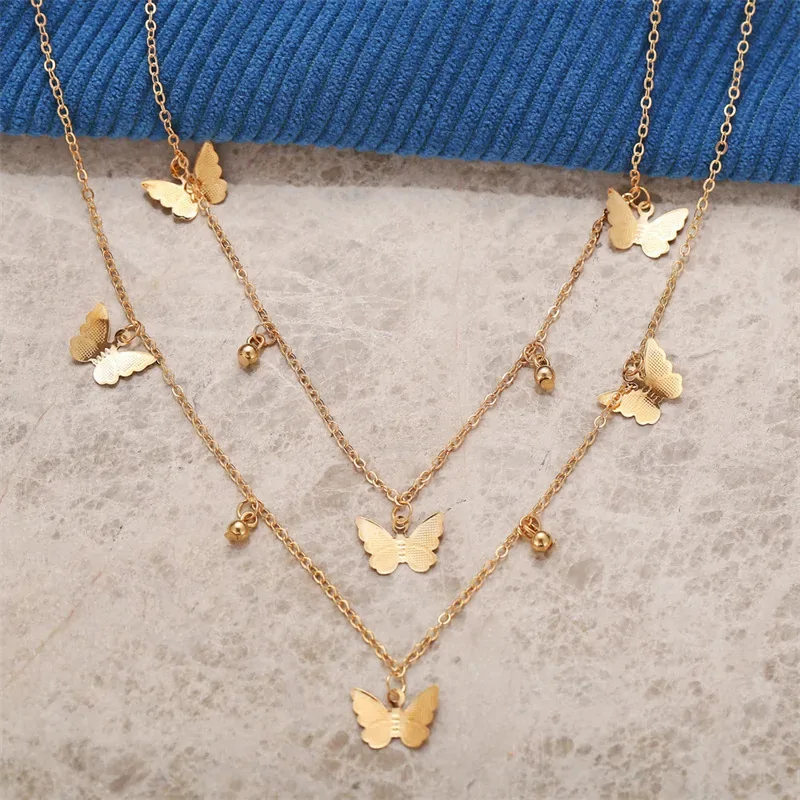 Collier à breloques papillon doré posé à plat, chaîne courte et chaîne longue