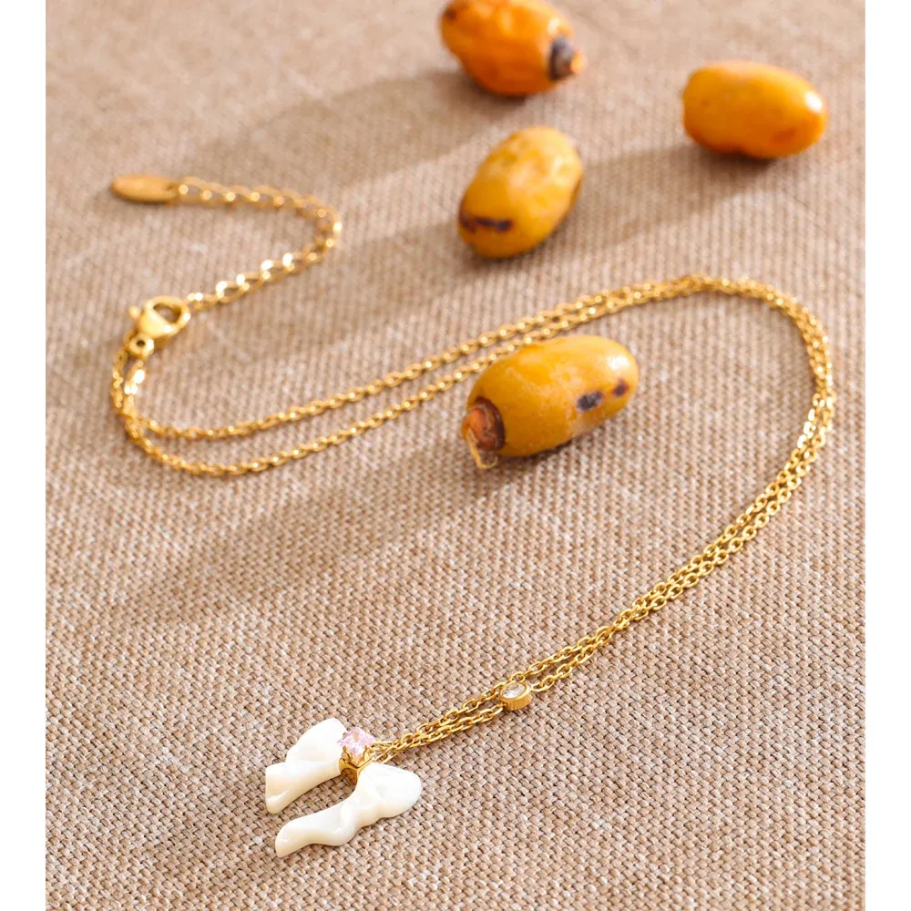 Collier nœud papillon en nacre naturelle et acier plaqué or, zircon rose central