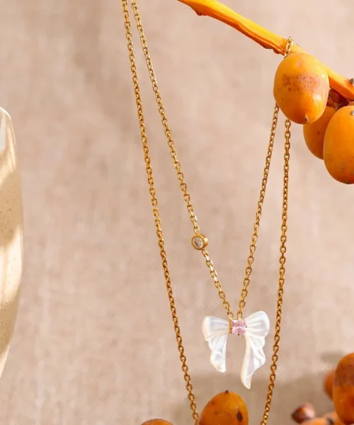 Collier nœud papillon en nacre naturelle et acier plaqué or, zircon rose central