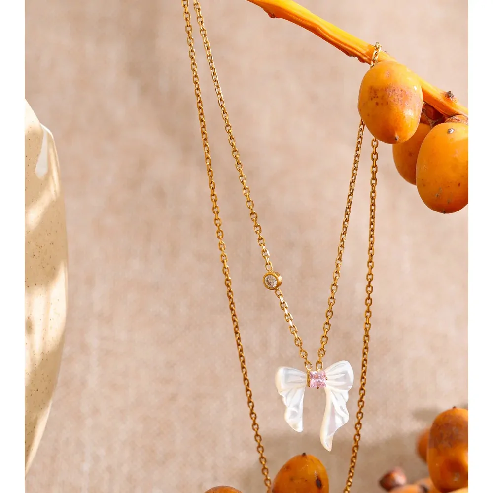 Collier nœud papillon en nacre naturelle et acier plaqué or, zircon rose central