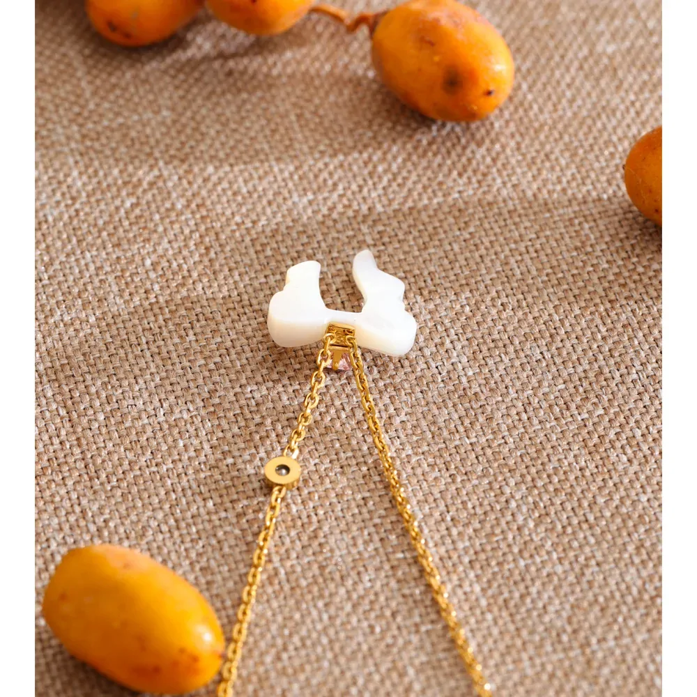 Collier nœud papillon en nacre naturelle et acier plaqué or, zircon rose central