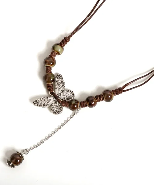 Détail du papillon argent vieilli enfilé sur cordon ciré entre des perles en céramique brunes